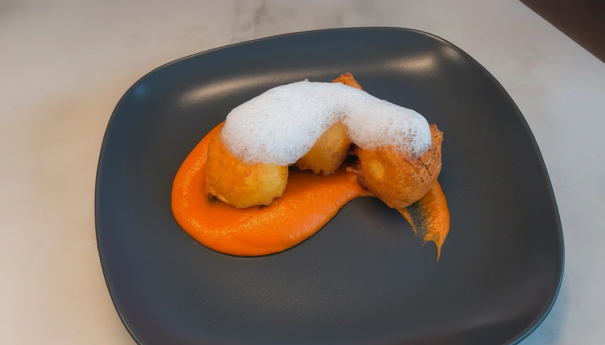 un plato de pizzara negro con buñuelos de mejillón en tempura con salsa brava casera
